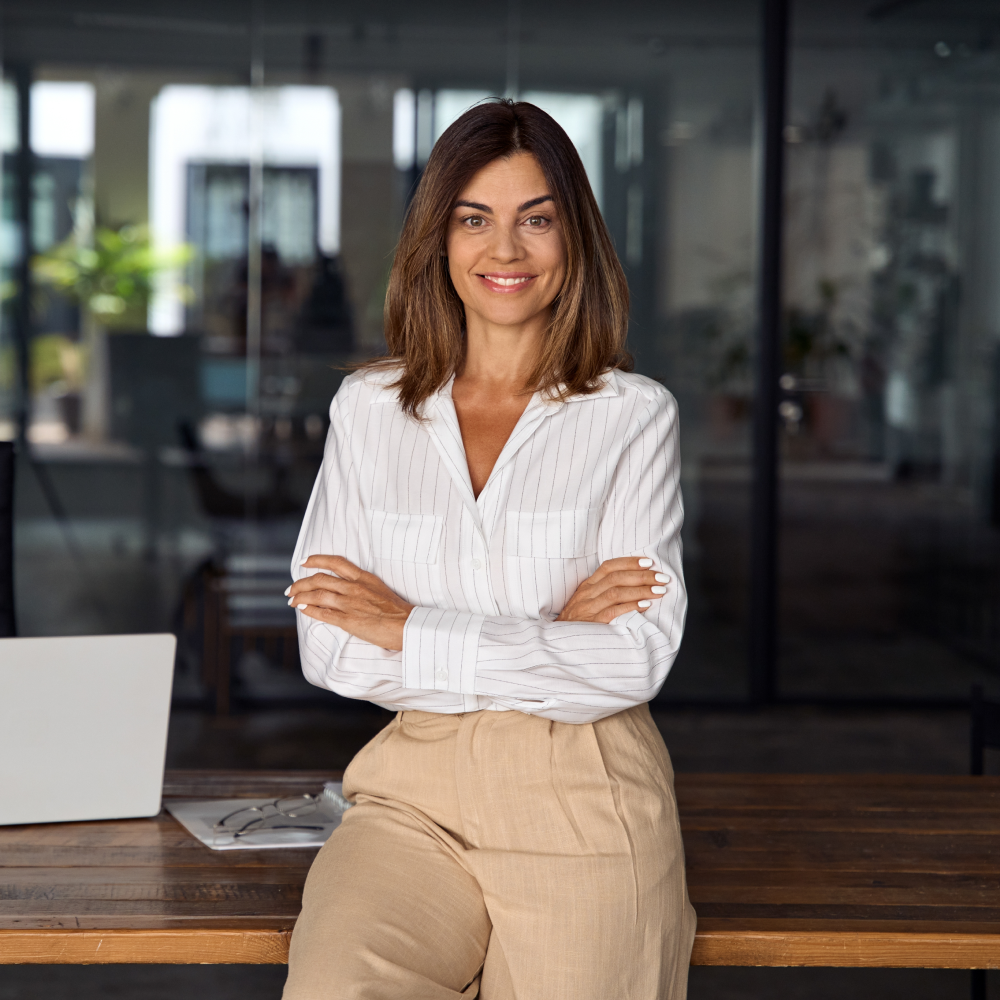 Woman is sitting on a desk, smiling with arms crossed